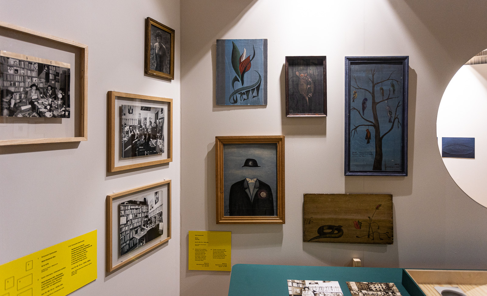 Zdjęcie wystawy „Prawobrzeżne”. Zdjęcia i obrazy w ramkach na ścianie, a przed stoi gablota z przedmiotami.